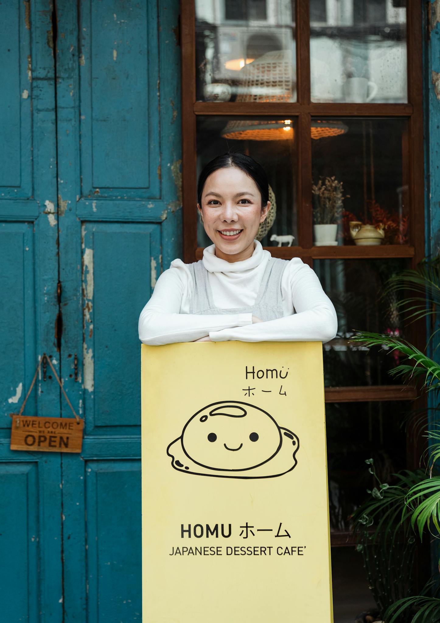A smiling woman stands at the entrance of a Japanese dessert cafe, exuding warmth and hospitality.
