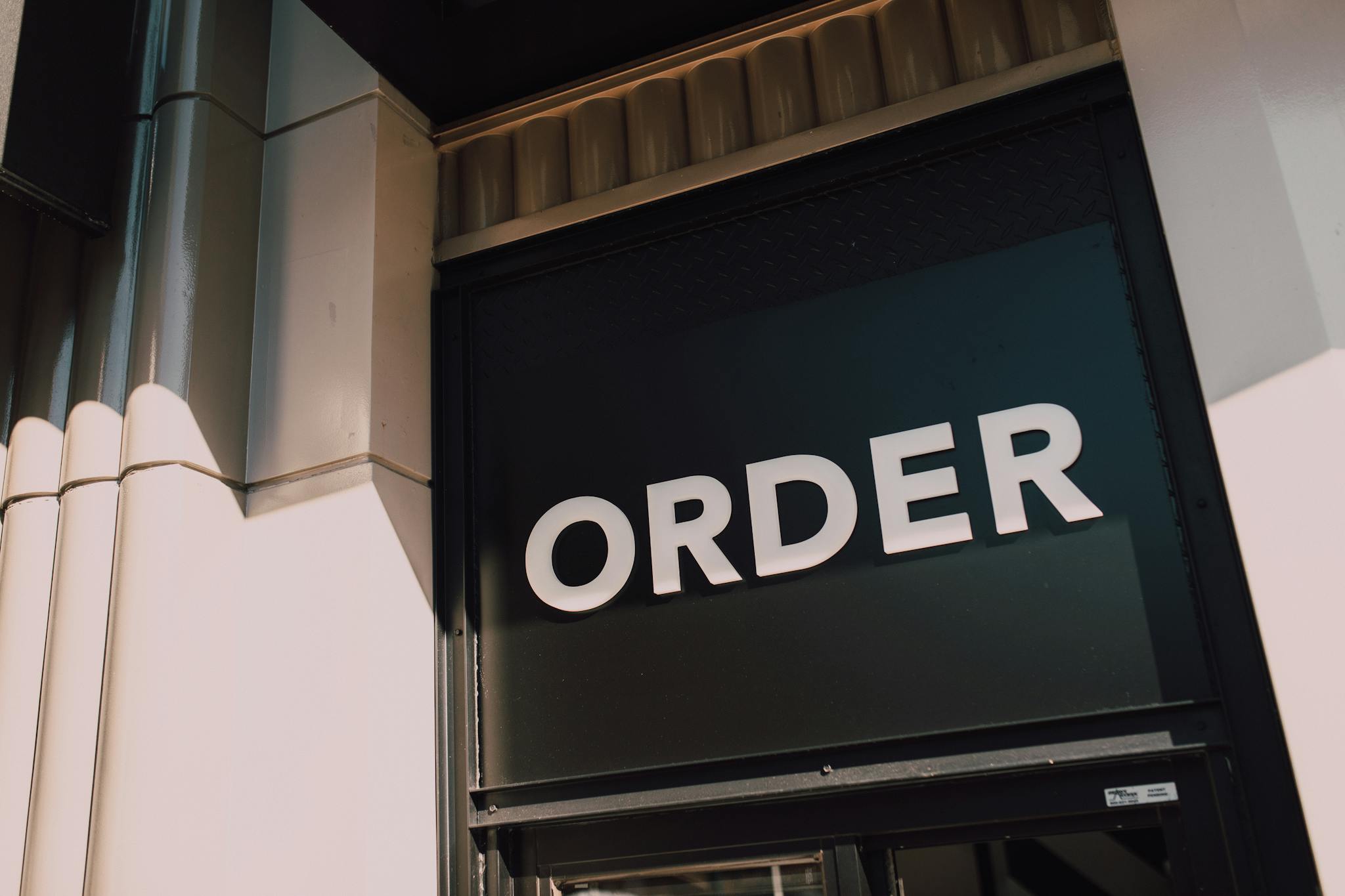 A sunlit view of a modern storefront with prominent 'Order' signage, highlighting a streamlined design.