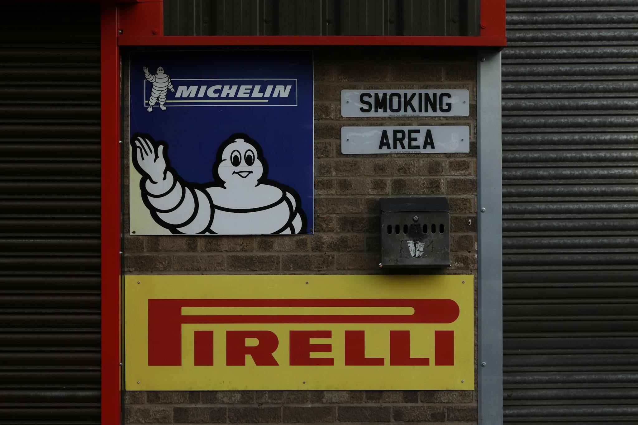 Industrial wall featuring Michelin and Pirelli signage with smoking area sign.